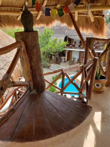 a wooden chair under a straw roof with a pool at Casa Hridaya Hotel Boutique in Holbox Island