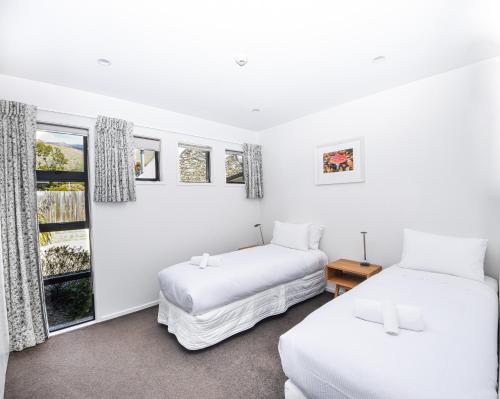 two beds in a room with white walls and windows at Tenby Apartments in Wanaka