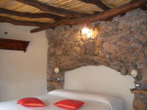 1 dormitorio con pared de piedra y 1 cama con almohadas rojas en Munduge b&b, en Lotzorai