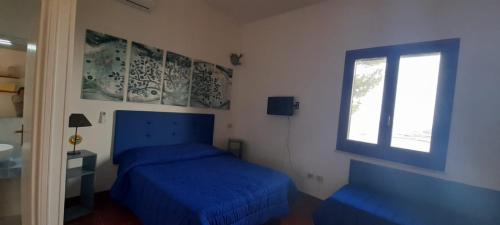 sypialnia z niebieskim łóżkiem i oknem w obiekcie La Pineta w mieście Favignana