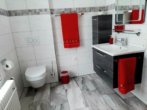 La salle de bains est pourvue de toilettes, d'un lavabo et de serviettes rouges. dans l'établissement Ferienwohnung Riedl, à Klingenthal