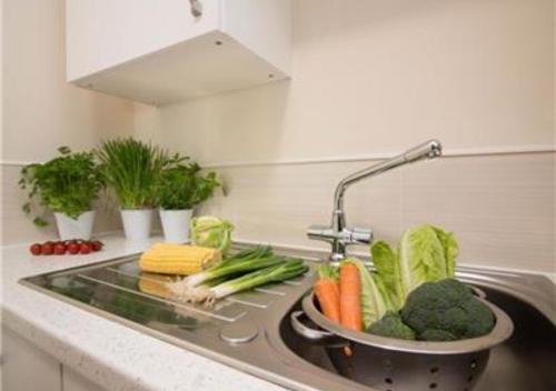 a kitchen counter with a sink with vegetables in it at StayZo Castle Point 18 Apartments - Premier Lodge in Southampton