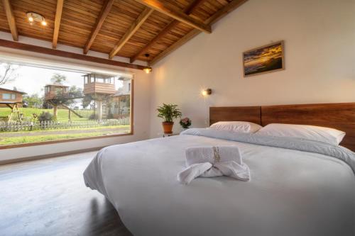 a large white bed in a bedroom with a large window at Hosteria Papagayo Cotopaxi in Machachi