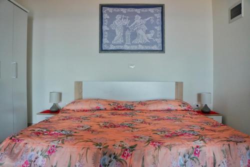een bed met een oranje dekbed en een foto aan de muur bij Apartmani Vesna in Zambratija