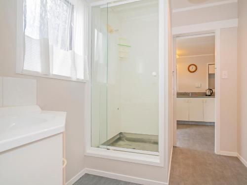 a glass shower in a white bathroom with a window at Daze Away - Cooks Beach Holiday Home in Cooks Beach