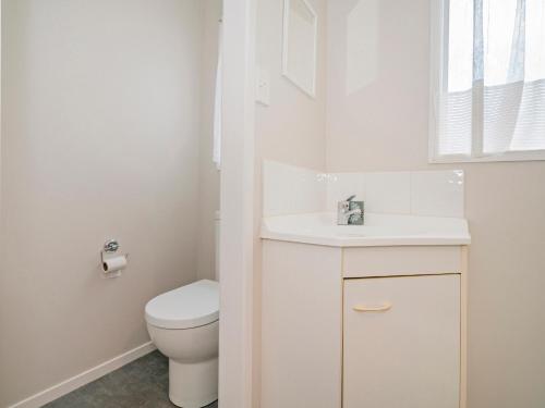 a white bathroom with a toilet and a sink at Daze Away - Cooks Beach Holiday Home in Cooks Beach