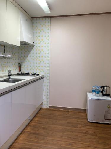 a kitchen with white cabinets and a sink and a refrigerator at HY Choi Hostel in Seogwipo