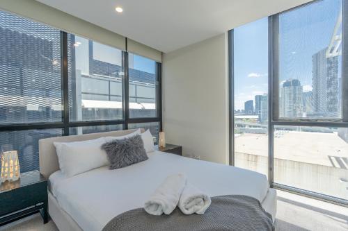 a bedroom with a white bed and large windows at Melbourne City Apartments - Teri in Melbourne