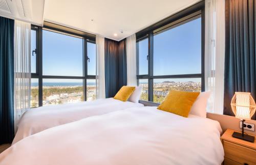 two beds in a bedroom with large windows at Ventimo Hotel & Residence Jeju in Jeju