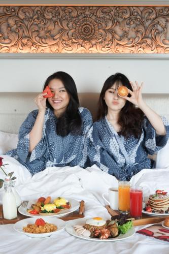 two women sitting in bed with plates of food at Shangri-la Surabaya in Surabaya