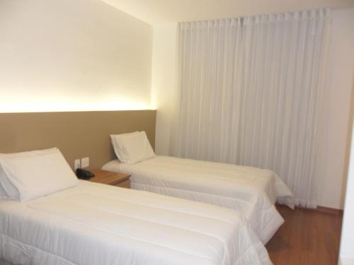 duas camas num quarto de hotel com lençóis brancos em Lord Hotel Aeroporto Confins em Vespasiano