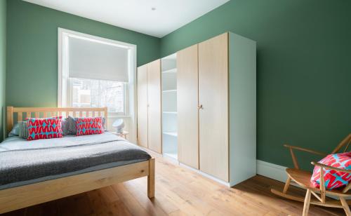 a bedroom with green walls and a bed with red pillows at The Notting Hill Escape - Modern & Bright 3BDR Flat with Balcony in London