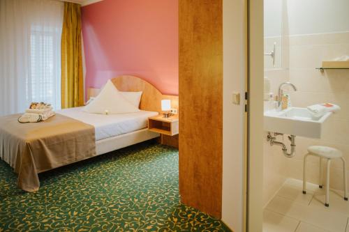 a bedroom with a bed and a bathroom with a sink at Kulturhotel Fürst Pückler Park in Bad Muskau