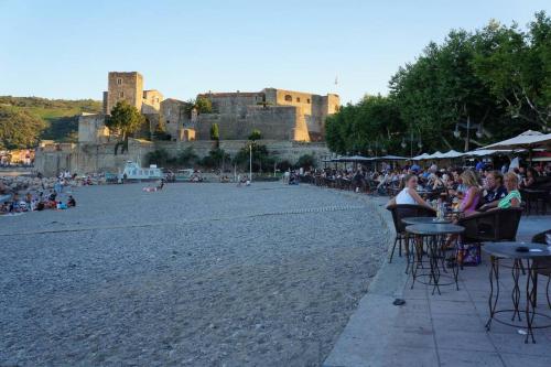 a group of people sitting at tables on a beach with a castle at Collioure Centre Ville, Calme, Clim in Collioure