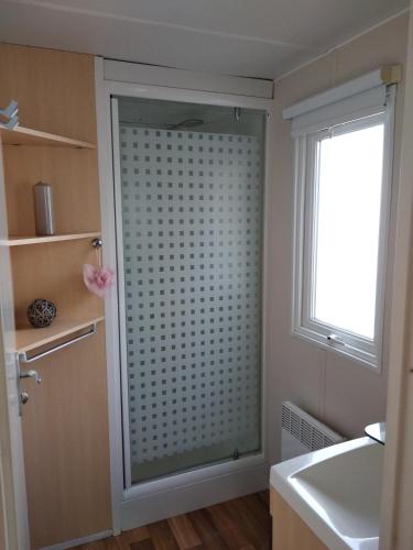 La salle de bains est pourvue d'une porte de douche en verre à côté d'une fenêtre. dans l'établissement Camping Parc des 7 Fonts, à Agde