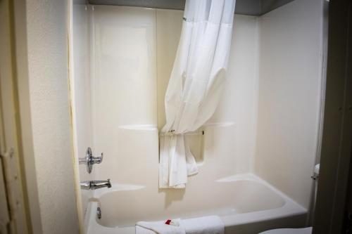 Days Inn by Wyndham Wagoner في Wagoner: حمام أبيض مع حوض استحمام ودش مع ستائر بيضاء