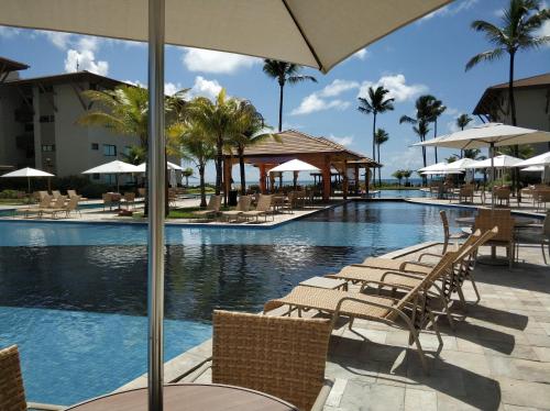 een zwembad met stoelen en tafels en een parasol bij Polinésia Resort Beira Mar Muro Alto Porto de Galinhas in Porto De Galinhas
