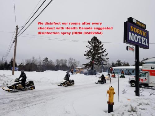 a group of people riding down a snow covered street on snowmobiles at Norvic Motel in Coniston