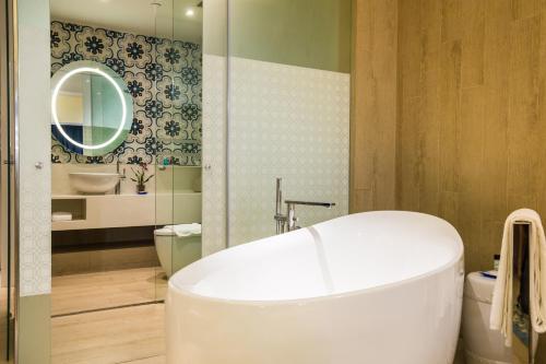 a bathroom with a tub and a toilet and a mirror at Village Hotel Katong by Far East Hospitality in Singapore