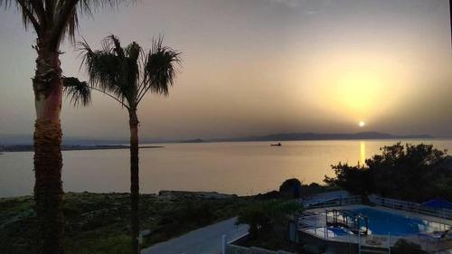 a sunset over a body of water with two palm trees at Nostalgia Villas in Tersanas