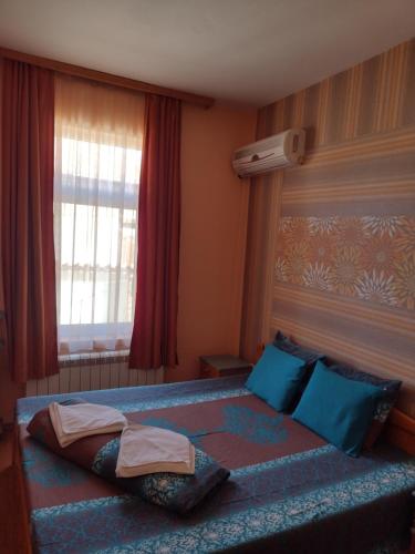 a bedroom with a bed with blue pillows and a window at Guest House Gergevana in Velingrad