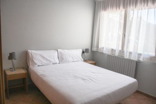 a bedroom with a bed with white sheets and a window at APARTAMENTS COLELLS in Bordes d´Envalira