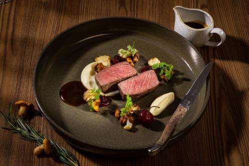 a plate of food with meat and vegetables and a knife at Schwarzer Adler Kitzbühel - Adults Only in Kitzbühel
