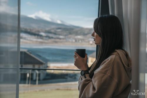 a woman holding a coffee cup looking out a window at Lake Hill Karkonosze Apartments in Sosnówka