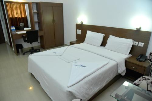 a bedroom with a large white bed and a desk at Emporium Hotel in Mangalore