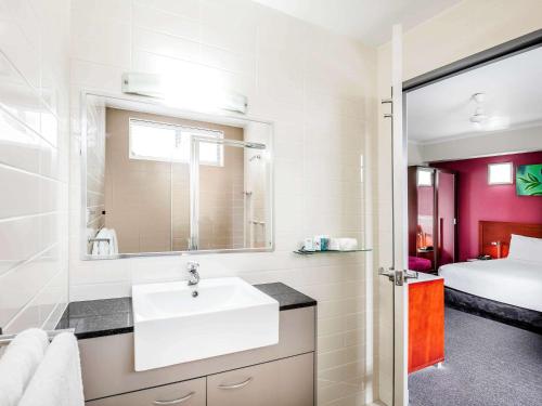 a white bathroom with a sink and a bed at Novotel Darwin Airport in Darwin