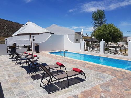 eine Gruppe von Stühlen und einem Sonnenschirm neben einem Pool in der Unterkunft Karoo 1 Hotel Village in De Doorns