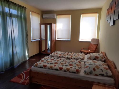 a bedroom with two beds and a chair and windows at Ponty Orsó Vendégház in Nagybaracska