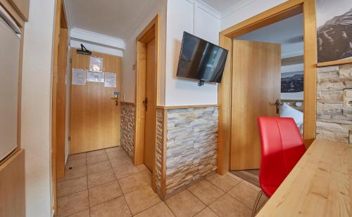 a room with a red chair and a television on the wall at Ski & Bike Appartements Forsthaus in Saalbach Hinterglemm