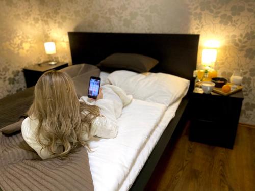 a woman laying on a bed holding a cell phone at Hotel Modena in Bratislava