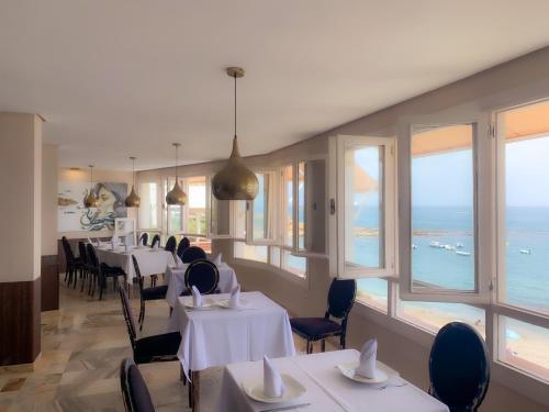 a dining room with white tables and chairs and windows at Hotel Patricia in Torreguadiaro