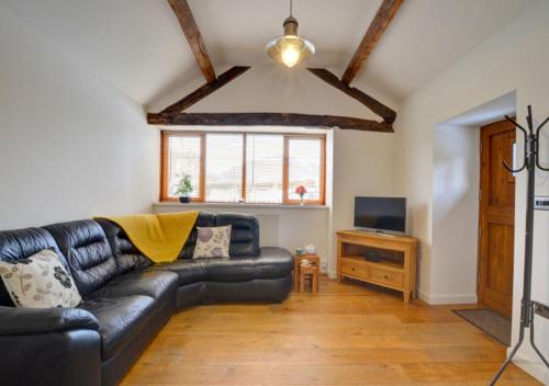 a living room with a black leather couch and a television at Smithy Cottage in Berriew