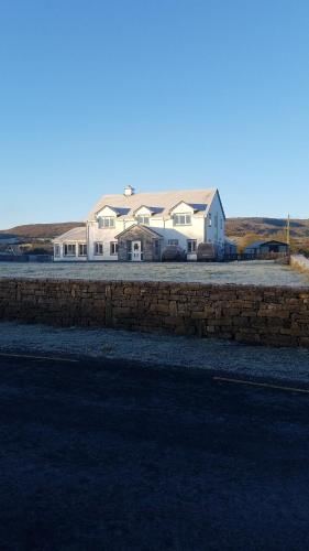 Cette grande maison blanche est dotée d'un mur en pierre. dans l'établissement Burren Rock Farmhouse B&B, à Turlough
