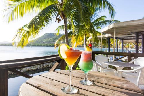 a wooden table with two drinks on a table with the ocean at St. James's Club Resort - All Inclusive in English Harbour Town