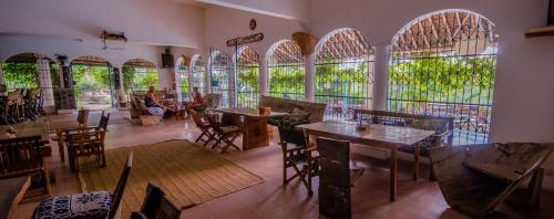 un ristorante con tavoli, sedie e ampie finestre di Distant Relatives Ecolodge & Backpackers a Kilifi