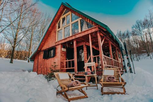 a log cabin in the snow with two chairs at Koliba Šume Pjevaju - robinzonski smjestaj, struja 12 V, voda iz cisterne in Mrkopalj