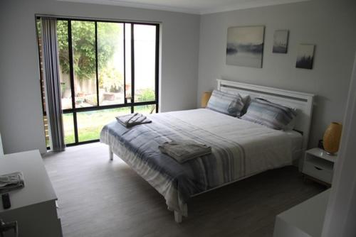 a white bedroom with a bed and a large window at Warnbro Beach Family Accommodation in Warnbro