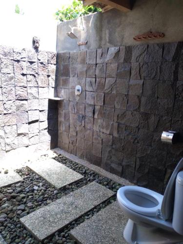 a bathroom with a toilet and a stone wall at Java Turtle Lodge Meru Betiri in Banyuwangi
