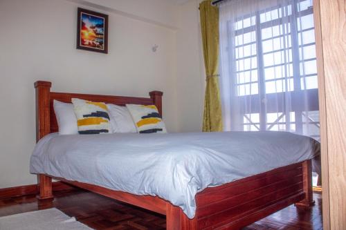een slaapkamer met een houten bed met kussens en een raam bij Kasty T Apartments- W Place in Nairobi