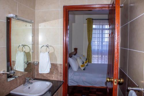 een badkamer met een wastafel en een spiegel en een bed bij Kasty T Apartments- W Place in Nairobi
