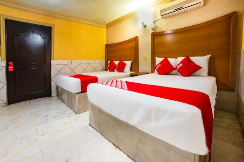 two beds in a hotel room with red pillows at Hotel San Marcos in Los Mochis