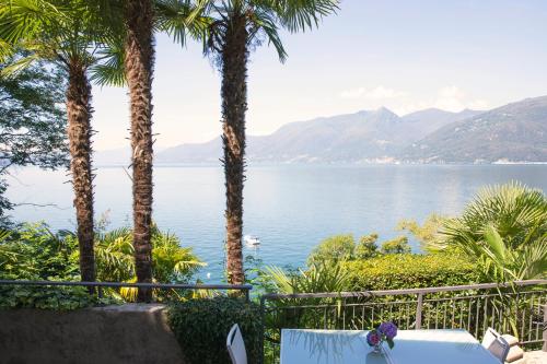 a table and chairs with palm trees and a body of water at CHARMING MOMENT di Villa Porta - Residenza Leonardo in Luino