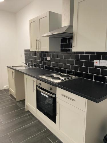 a kitchen with white cabinets and a black counter top at Nantwich House in Crewe