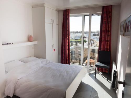 a white bedroom with a bed and a balcony at Appartementen Bredene in Bredene-aan-Zee