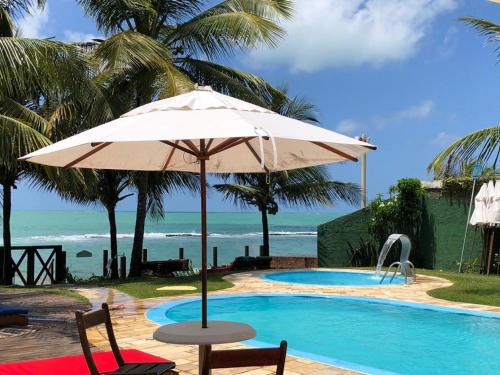 una sombrilla sentada junto a una piscina con el océano en Apart Hotel Praia dos Carneiros Apto 101 en Praia dos Carneiros