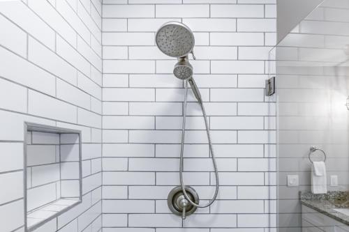a shower head in a white tiled bathroom at Explore Historic DT In This Cozy Open Air 5BR Stay in Cartersville